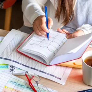 Hands writing in planner with coffee and glasses